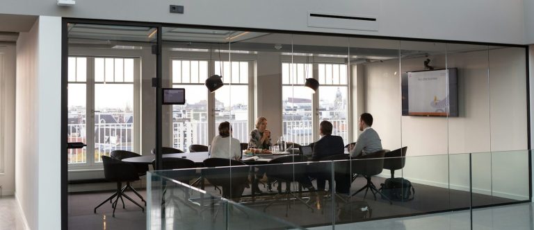 Gründungsberatung mit Weitblick Besprechungsraum mit vier Personen und Blick auf die Stadt durch große Fenster.