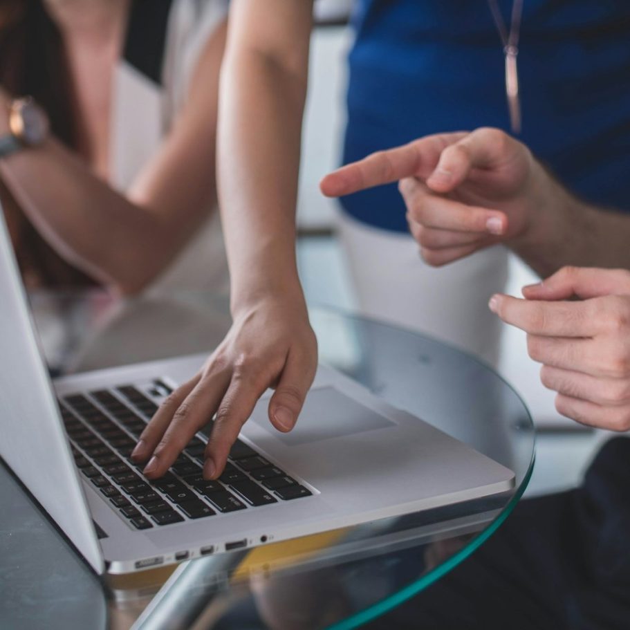 Wir helfen dir mit deinem Business! Hände von mehreren Personen, die auf einen Laptop-Bildschirm zeigen und diskutieren.